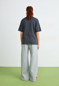 Pelēks oversized t-krekls ar īsām piedurknēm, kombinēts ar platām pelēkām sporta biksēm. Gluda auduma, brīva silueta un minimāli detalizējumi.