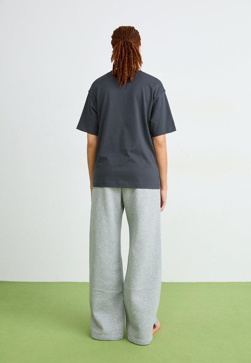 Graues, übergroßes T-Shirt mit kurzen Ärmeln, kombiniert mit weiten grauen Jogginghosen. Glattes Material, lockere Passform und minimale Details.