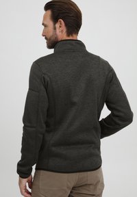 Menns mørkegrå fleecejakke med høy krage, teksturert stoff og lange ermer; har ribbede detaljer og en tettsittende design.