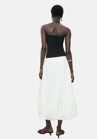 Schwarzes trägerloses Oberteil, kombiniert mit einem weißen, voluminösen Maxirock mit gerafftem Saum. Das Model trägt flache schwarze Sandalen und minimale Accessoires.