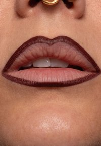 Labbra di un tenue rosa circondate da una matita labbra marrone scuro, con un prominente arco di Cupido e denti visibili, accentuati da un anello al naso.
