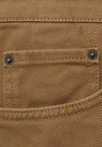 Tissu marron avec une texture à armure en diagonale, présentant une poche à rabat avec deux boutons métalliques et des bords cousus pour une meilleure durabilité.