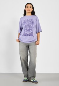 Purple graphic t-shirt featuring a sun design and text "LE SOLEIL," paired with light gray wide-leg jeans and multicolored sneakers.