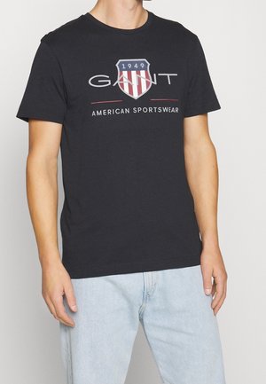 Zwart katoenen t-shirt met een schildlogo met rood-witte strepen en de tekst "GANT 1949 AMERICAN SPORTSWEAR." Korte mouwen en een ronde hals.