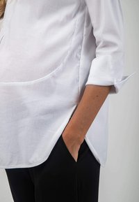 White shirt with three-quarter sleeves, featuring a round hem, and a pocket on the side. Paired with black textured pants.