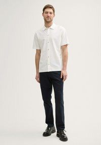 Kortärmad witten blouse met een gestructureerde stof, gecombineerd met donkerblauwe broek en zwarte dresschoenen, dat een casual uitstraling toont.