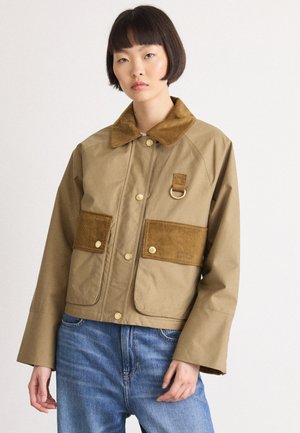 Bruine jas met een corduroy kraag en zakken, voorzien van goudkleurige hardware en een gestructureerde stof, gecombineerd met lichtblauwe jeans.