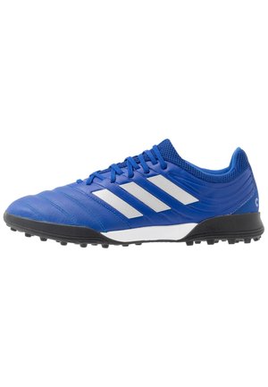 Chaussure de football bleue avec des bandes blanches Adidas, semelle noire avec des crampons et lacets bleus, vue de côté extérieur sur fond blanc.
