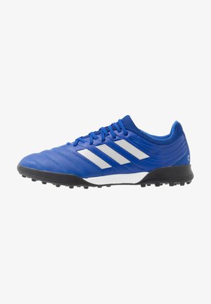 Chaussure de football bleue avec des bandes blanches Adidas, semelle noire avec des crampons et lacets bleus, vue de côté extérieur sur fond blanc.