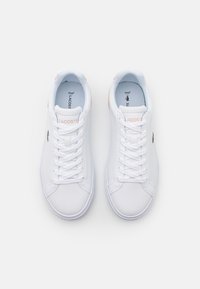 Baskets en cuir blanc avec un design à lacets, dotées d'un embout arrondi, d'accents texturés et d'un petit logo de crocodile vert sur le côté.