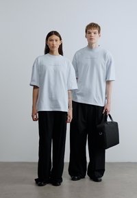 Ανοιχτό μπλε φαρδιά μπλουζάκια με κοντά μανίκια, σε συνδυασμό με μαύρο παντελόνι φαρδιάς γραμμής. Ο άνδρας μοντέλο κρατάει μια μαύρη τσάντα με μεταλλικό δαχτυλίδι ως διακοσμητικό.