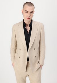 Šviesiai smėlio spalvos dvigubos eilės kostiumo švarkas su tekstūruotu paviršiumi, derinamas su juoda marškiniais su raštuota apykakle. Stilingas, slim fit dizainas.