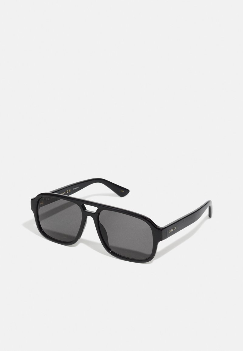 Gafas de sol rectangulares negras con lentes oscuros sólidos, marco de plástico brillante y un sutil diseño en dorado en las patillas.