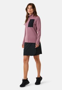 Fleece zip-up jacket in mauve with black chest pocket, paired with a black skort. Features long sleeves and a fitted design.