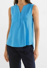 Blå ärmlös blus med två bröstfickor, V-ringning, sidoklippor och en slät textur, tillverkad av lättviktsmaterial.