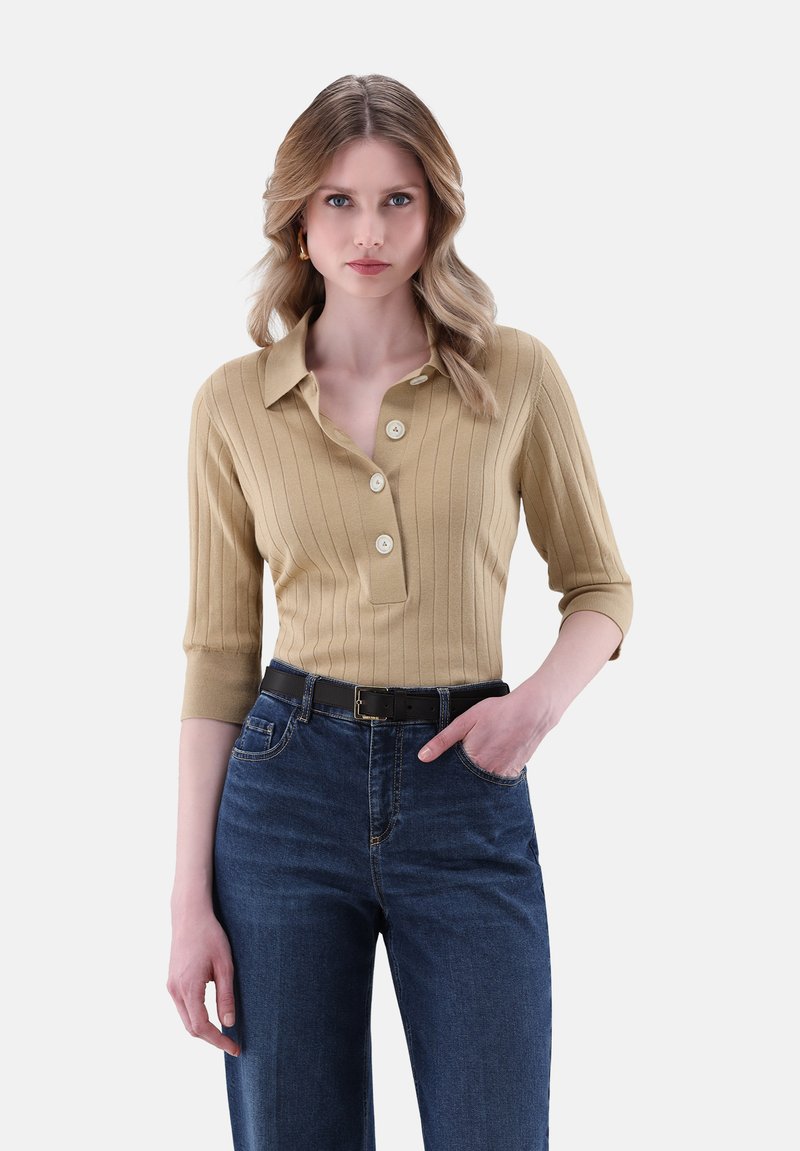 Beige Strickoberteil mit gerippter Textur, Kragen, drei Knöpfen und 3/4-Ärmeln, kombiniert mit dunkelblauen weit geschnittenen Jeans und einem schwarzen Gürtel.