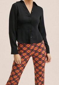 Chemise noire à manches longues avec fermeture à boutons et col, associée à un legging coloré à motifs floraux dans des teintes de rose, orange et vert.