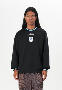 Sort sweatshirt med rund hals, lyseblå accenter og et broderet logo på brystet. Blødt stof og løs pasform.