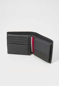 Portefeuille en cuir noir avec plusieurs emplacements pour cartes, une poche centrale et un détail rayé rouge et blanc en contraste. Texture lisse et design minimal.