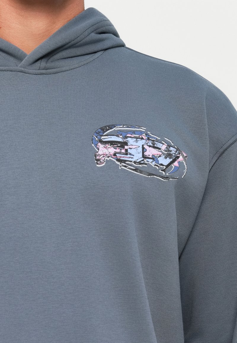 Sudadera gris con un diseño gráfico texturizado en azul y rosa en la zona del pecho, con un estilo clásico de pull-over y una tela suave.