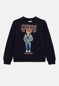 Μαύρο φούτερ με γραφικό αρκούδας με τζιν ντύσιμο, με την επιγραφή «GUESS» κόκκινη πάνω και «AUTHENTIC DENIM BRAND» κάτω.