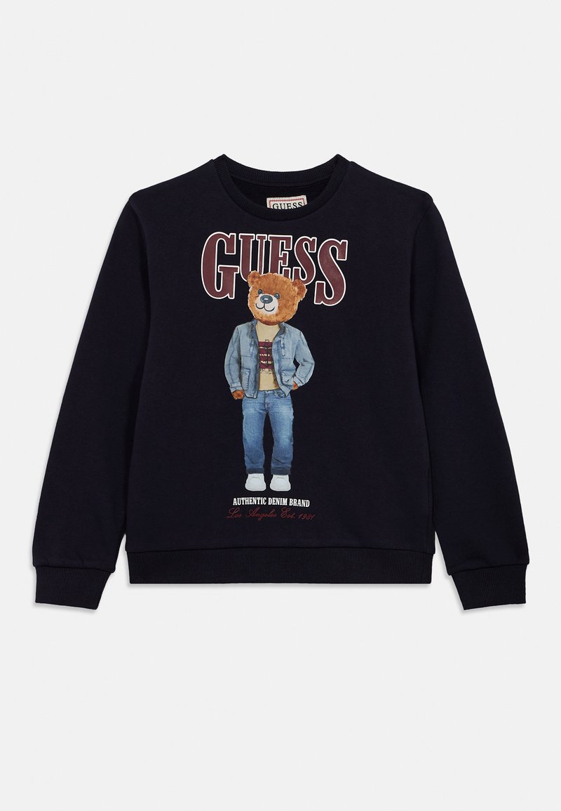 Μαύρο φούτερ με γραφικό αρκούδας με τζιν ντύσιμο, με την επιγραφή «GUESS» κόκκινη πάνω και «AUTHENTIC DENIM BRAND» κάτω.