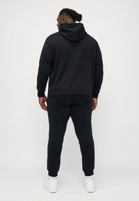 Schwarzer Hoodie mit einer Kängurutasche und einer Kapuze mit Kordelzug, kombiniert mit passenden Jogginghosen. Glattes Material, gerippte Bündchen und Knöchel.