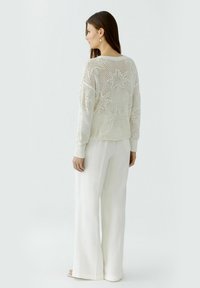 Leichter Strickpullover in Off-White mit Sternenmuster. Besitzt einen lockeren Schnitt, lange Ärmel und gerippte Bündchen. Kombiniert mit weit geschnittenen weißen Hosen.
