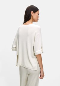 Jasno beżowy, oversize sweter z rękawami z mankietem, o mi�ękkiej fakturze i bocznych rozcięciach, przedstawiony z tyłu na jednolitym tle.