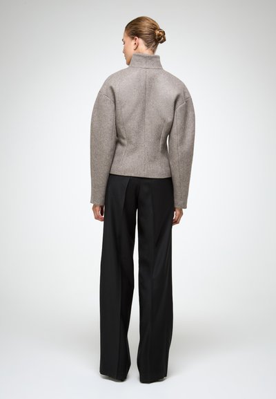 Siva jakna od vune s visokim ovratnikom i strukturiranim ramena, uparenim s crnim hlačama širokih nogavica. Glatka tekstura, prilagođen kroj.