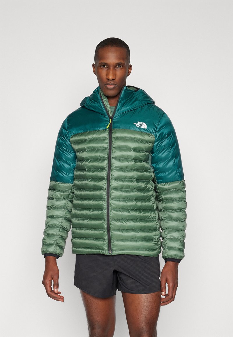 Hooded jack met een groene en teal kleurenschema, gewatteerd puffer ontwerp, synthetisch materiaal en een rits aan de voorkant. Logo op de borst.