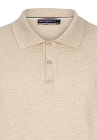 Beige polo särk tekstuuriga mesilaste kärje mustriga, kolme nupuga avamine ja pehme kudumiga krae. Sildil on kirjas "FELIX HARDY."