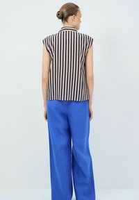 Gestreifte Bluse in Marineblau und Pfirsich, mit kurzen Ärmeln und Kragen, kombiniert mit lockeren blauen Leinenhosen. Glatte Textur und taillierte Passform.
