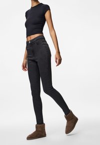 Úzké černé džíny, přiléhavý černý krátký top s krátkými rukávy a hnědé semišové kotníkové boty. Oblečení má hladkou texturu a jednoduchý design.