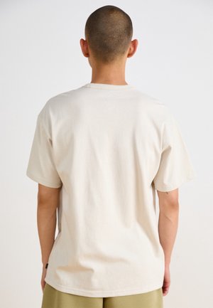 Béžové bavlněné tričko s krátkým rukávem a kulatým výstřihem. Jednoduchý design, uvolněný střih, zadní pohled ukazuje hladkou strukturu a jednoduché švy.