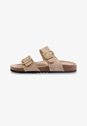 Sandale slip-on couleur cuir clair avec deux brides réglables à boucle, détails clous dorés, semelle intérieure en liège et semelle extérieure en caoutchouc noir.