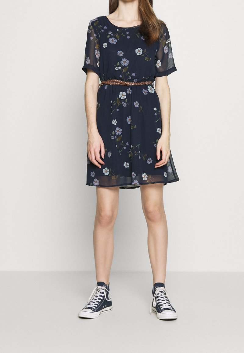 Robe à imprimé floral bleu marine avec manches courtes transparentes, taille cintrée et coupe décontractée. Associée à des baskets hautes pour un look casual.