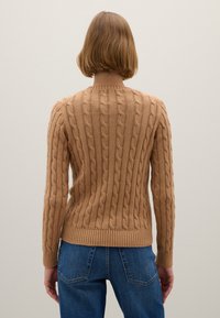 Suéter de punto acanalado en marrón claro, con patrones texturizados, un dobladillo acanalado y mangas largas. Combinado con jeans de mezclilla azul.