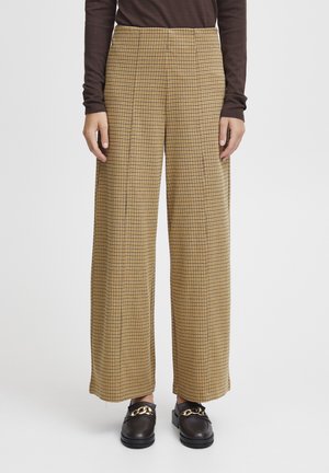 Pantaloni a gamba larga a quadri gialli e neri, con vita alta e una texture liscia, abbinati a scarpe slip-on scure.