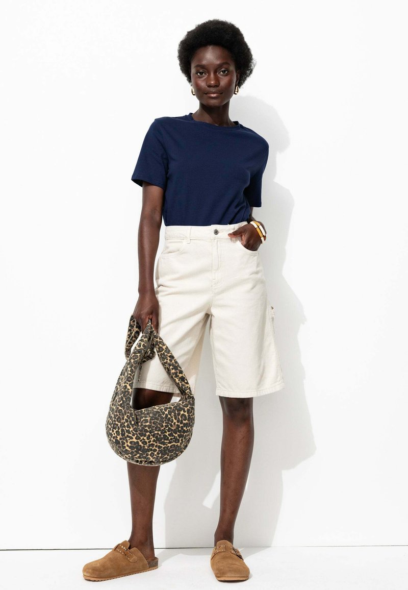 T-shirt marine à manches courtes, short cargo beige décontracté, chaussures brunes à enfiler et sac à motif léopard marron. Tenue simple et décontractée.