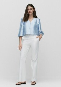 Ljusblå satin crop top med V-ringning, puffärmar, matchad med vita raka byxor och svarta sandaletter med remmar.