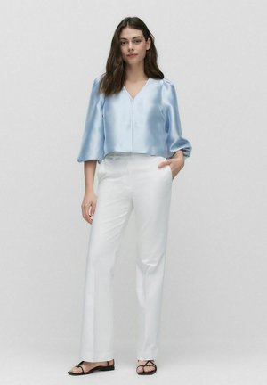 Himmelblaues Satin-Crop-Top mit V-Ausschnitt und Puffärmeln, kombiniert mit weißen geraden Hosen und schwarzen Riemchensandalen.