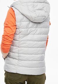 Grijze puffer vest met een capuchon, met een horizontaal geborduurd ontwerp en een hoge kraag, gelaagd over een oranje langemouwenshirt.