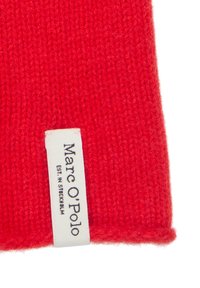 Rode gebreide muts met een zachte textuur en een omgeslagen rand, met een wit label waarop "Marc O'Polo" en "Est. in Stockholm." staan.