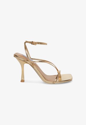Sandales à talons hauts dorées métalliques avec un bout carré, une fine sangle de cheville et des lanières croisées à l'avant ; texture lisse et design épuré.