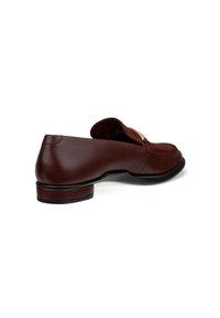 Mocassin en cuir marron avec un bout arrondi et un petit talon. Présente une sangle décorative et des matériaux en métal doré à l'avant.