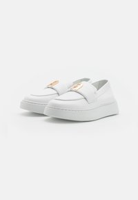 Scarpe slip-on bianche in pelle liscia con un logo geometrico in rilievo sulla striscia e una spessa suola bianca a piattaforma.