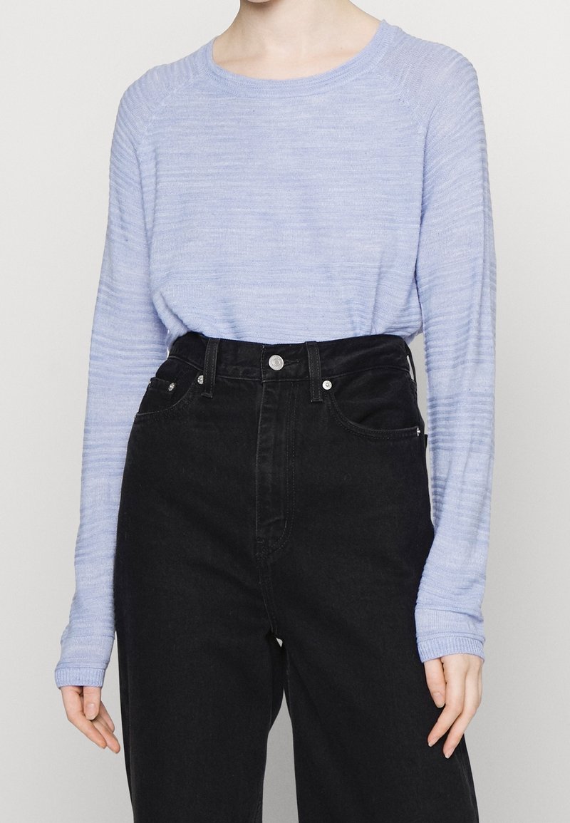 Hellblau gestrickter Pullover mit langen Ärmeln, rundem Halsausschnitt und feinen horizontalen Streifen, kombiniert mit hochgeschnittenen schwarzen Jeans.