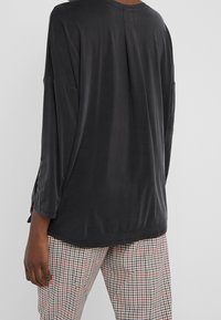 Schwarzes Langarmshirt mit entspannter Passform, runder Ausschnitt und weichem Stoff, kombiniert mit einer Hose im Karomuster mit roten Akzenten.