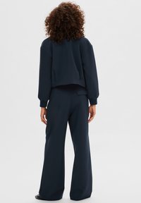 Sudadera corta de color navy con mangas anchas, combinada con pantalones de pierna ancha de cintura alta en tela a juego, con una textura suave.